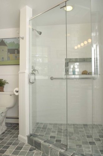 Glassed in, roomy corner shower. White subway tiles accented in deep grey to compliment the grey tile floor.